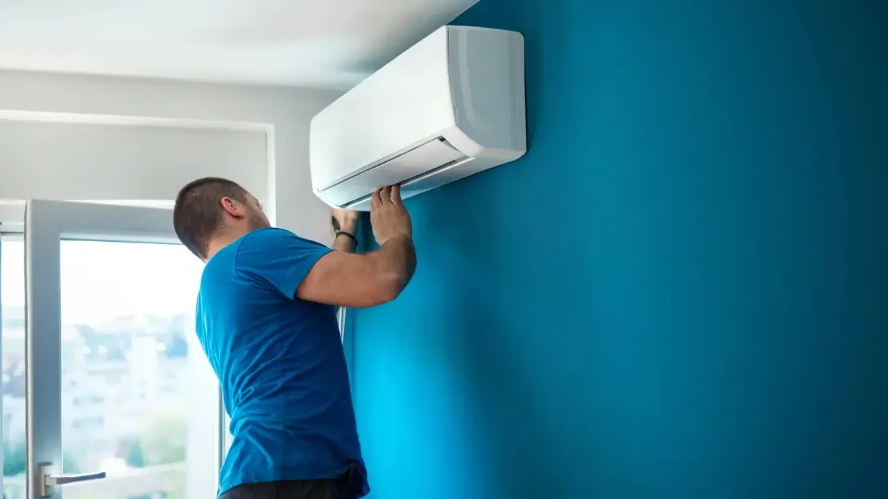 Técnico con carnet instalador aire acondicionado ajusta unidad interior en pared azul.