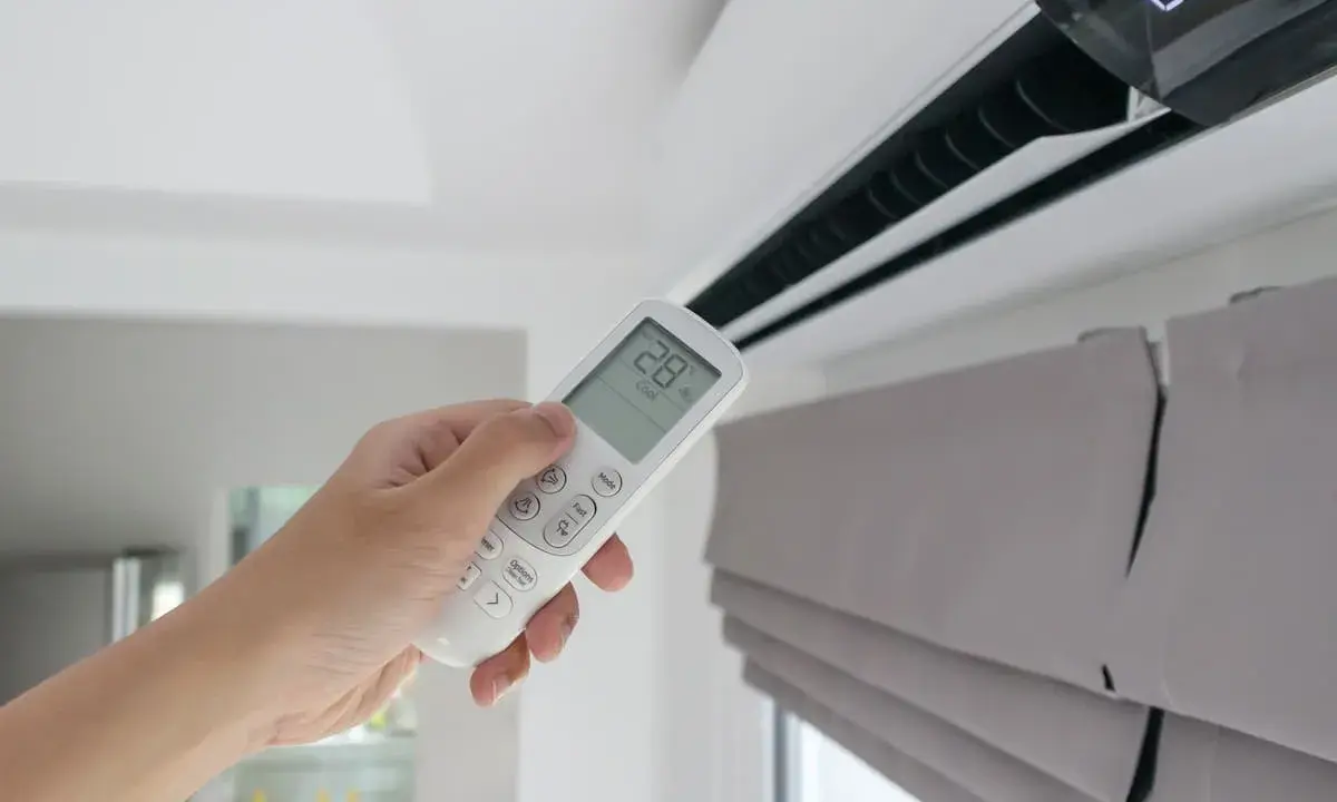 Mano sujetando control remoto de aire acondicionado, mostrando la diferencia entre climatizador y aire acondicionado.