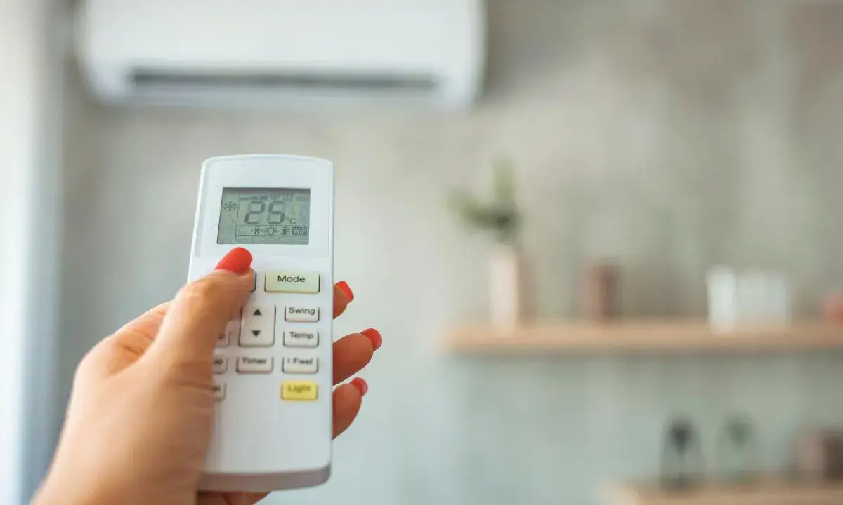 Mano con control remoto ajustando el aire acondicionado, buscando la temperatura ideal.