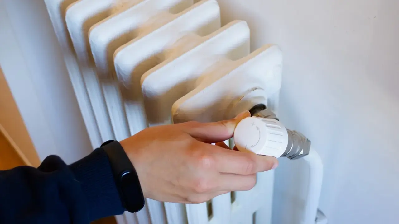 Mano ajustando el termostato de un radiador, controlando la calefacción central en comunidades de vecinos para un confort óptimo.