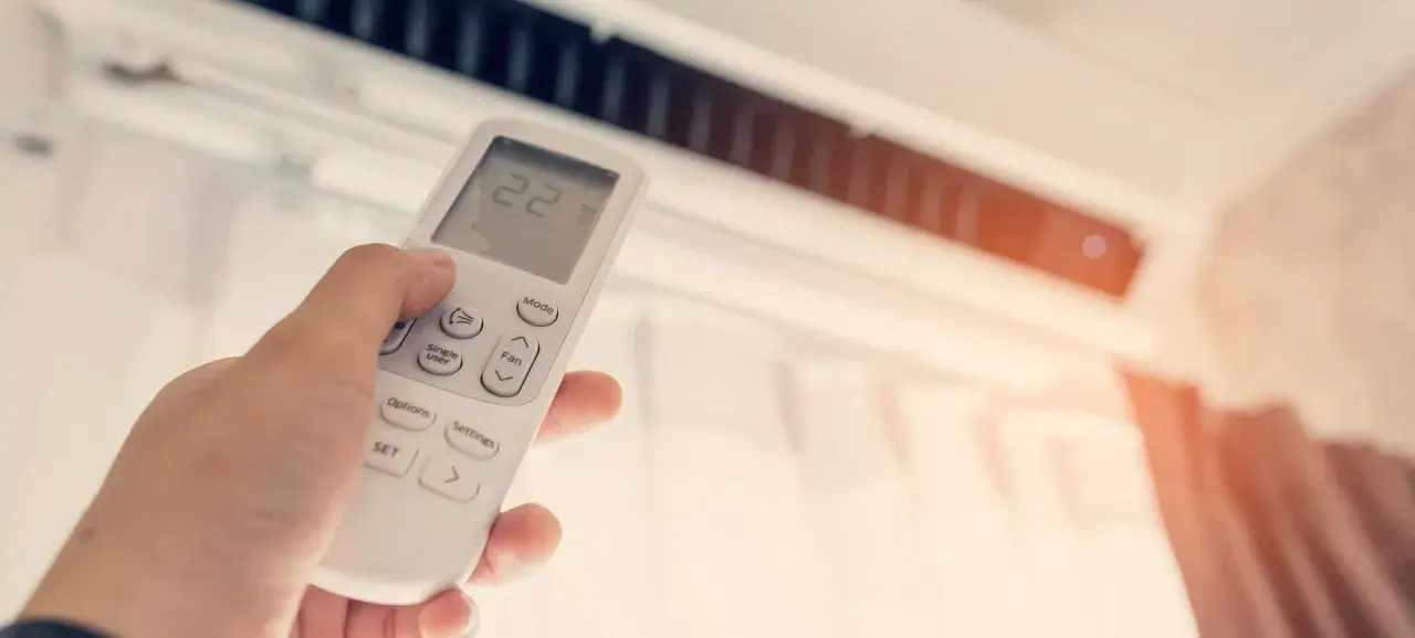 Mano ajustando el control remoto de un aire acondicionado, buscando la temperatura ideal en frigorías por m2 para un confort óptimo.