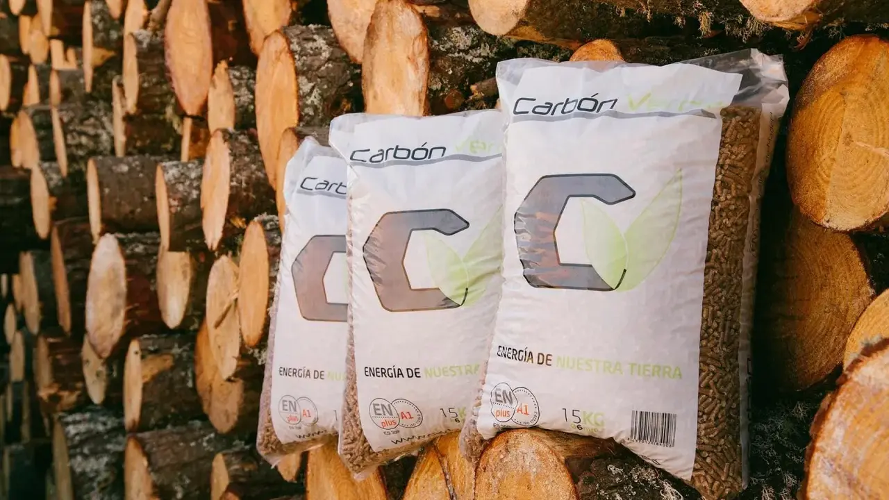 Bolsas de pellets de madera "Carbón Verde" apiladas contra troncos. Si tu estufa de pellets muestra un error 3, revisa la carga de combustible.
