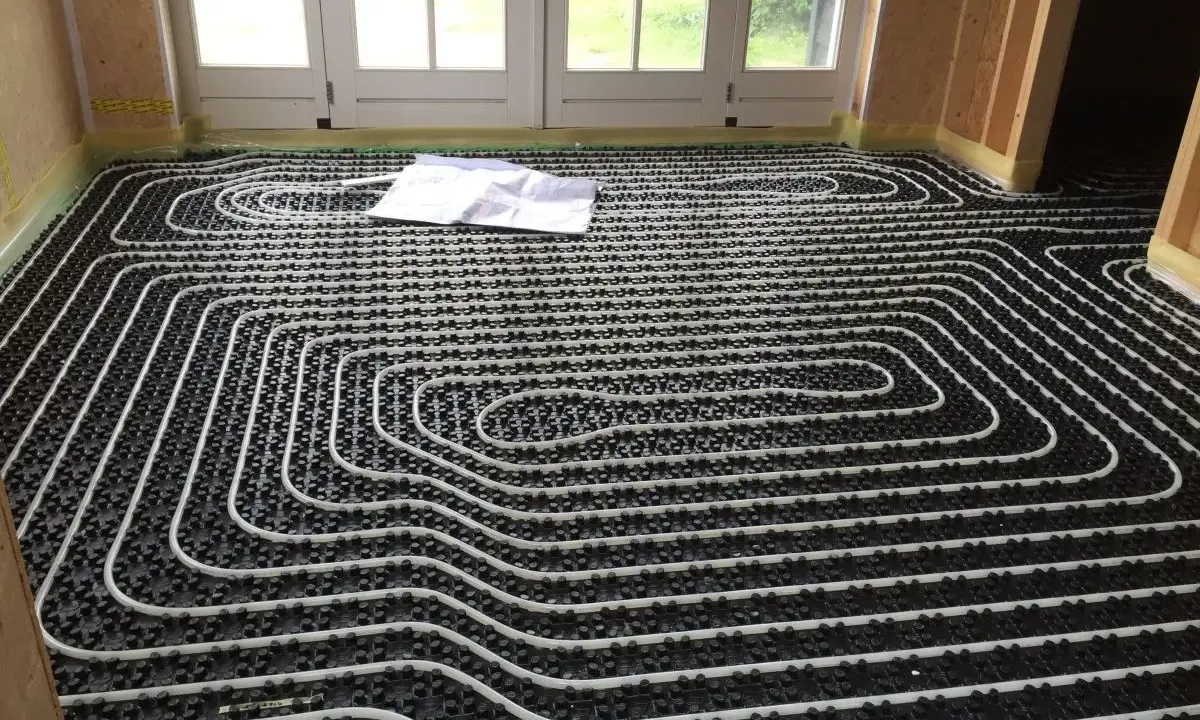 Instalación de tuberías blancas sobre paneles negros para un futuro suelo radiante. Un plano yace sobre el suelo.