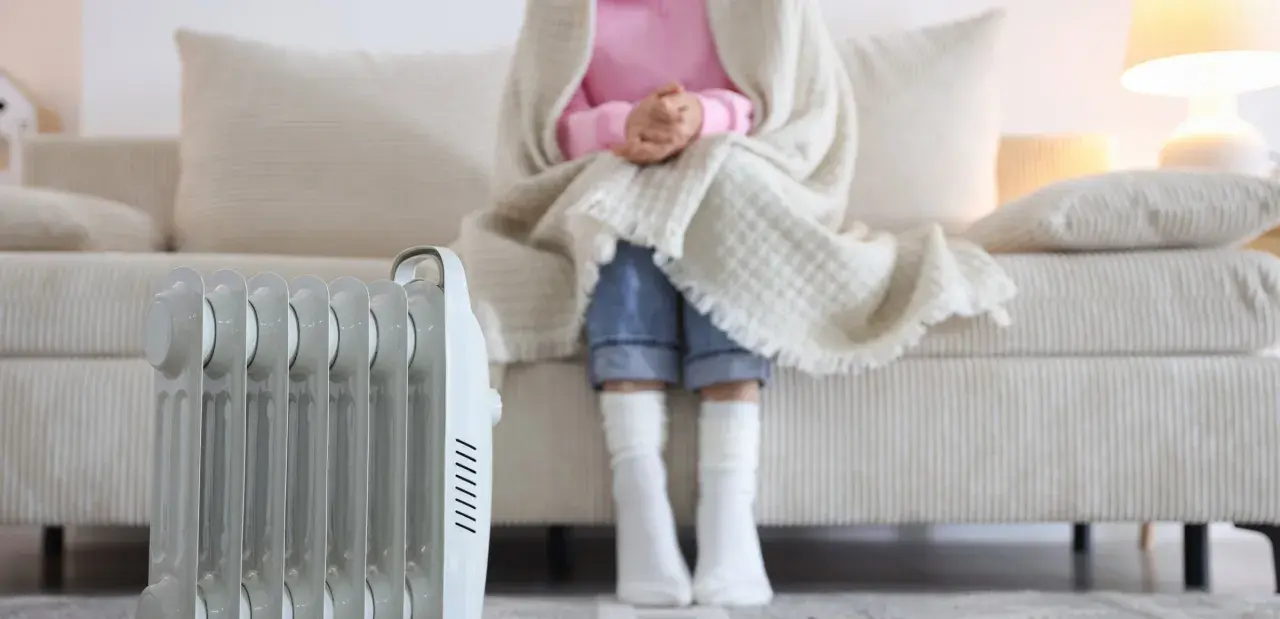 Radiador eléctrico junto a un sofá donde una persona se abriga. Una solución eficaz para los sistemas de calefacción del hogar.