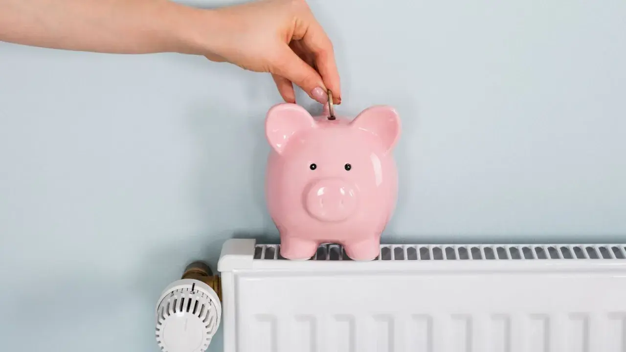 Mano inserta moneda en hucha rosa sobre radiador blanco. Ahorrando energía cuando se apaga la calefacción central.