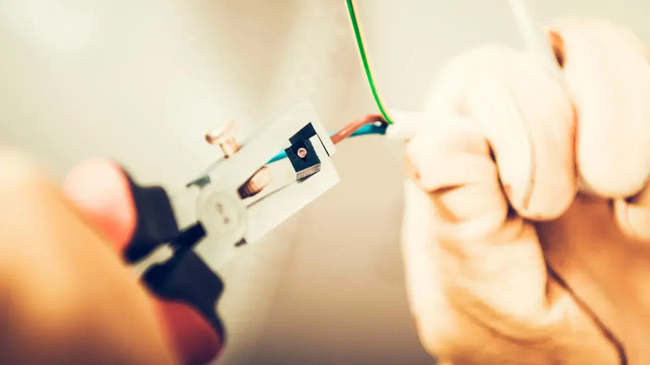 Manos con guantes pelando cables para como cambiar el termostato de la calefacción.