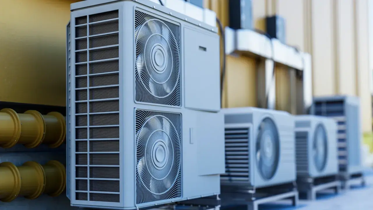 Unidades exteriores de aerotermia R290, con ventiladores y rejillas, alineadas junto a una pared amarilla y tuberías.