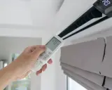 Mano sujetando control remoto de aire acondicionado, mostrando la diferencia entre climatizador y aire acondicionado.
