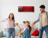 Familia feliz bailando bajo un aire acondicionado inverter rojo, disfrutando del confort y bajo consumo kwh.