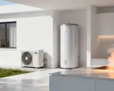 Unidad exterior de bomba de calor aerotermia junto a un termo acumulador. Vapor de agua sale de un grifo en la cocina.