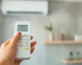 Mano con control remoto ajustando el aire acondicionado, buscando la temperatura ideal.