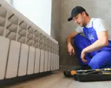 Técnico revisa la **presión de la caldera** junto a un radiador blanco. Herramientas a su lado.