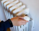 Mano ajustando el termostato de un radiador, controlando la calefacción central en comunidades de vecinos para un confort óptimo.