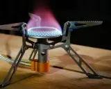 Estufa portátil sin electricidad ni gas, con llama azul y púrpura, ideal para acampar.