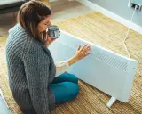 Mujer con taza de té cerca de un calefactor eléctrico, una solución para la alternativa al gas en un piso.