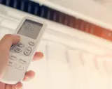 Mano ajustando el control remoto de un aire acondicionado, buscando la temperatura ideal en frigorías por m2 para un confort óptimo.