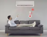 Hombre en sofá con control remoto ajustando el aire acondicionado calefacción. Termómetro rojo indica alta temperatura.