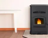 Estufa de pellets negra con fuego encendido. Junto a una mesa blanca. ¡No cae pellet en la estufa, todo limpio y seguro!