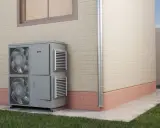 Unidad exterior de aire acondicionado para calefacción por inercia, instalada junto a una pared de ladrillo.