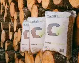 Bolsas de pellets de madera "Carbón Verde" apiladas contra troncos. Si tu estufa de pellets muestra un error 3, revisa la carga de combustible.