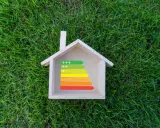 Casa de madera sobre césped con etiqueta de eficiencia energética, ideal para calefacción sostenible.