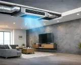 Un sistema fancoil integrado en el techo distribuye aire fresco en un salón moderno con sofá gris y TV.