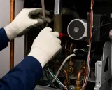 Técnico revisa el funcionamiento de una caldera, manipulando cables y tuberías de cobre.