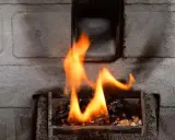 Llamas naranjas bailan sobre pellets en la estufa. El fondo de ladrillo gris sugiere que la alarma 6 estufa pellet está funcionando.