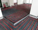 Instalación de suelo radiante aerotermia con tuberías rojas sobre paneles negros en una habitación en construcción.