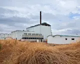 Planta de biomasa industrial con chimenea alta y torres de refrigeración, rodeada de vegetación seca.