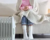 Radiador eléctrico junto a un sofá donde una persona se abriga. Una solución eficaz para los sistemas de calefacción del hogar.