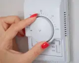 Mano ajustando el termostato para el cálculo de calefacción de la vivienda. La temperatura se muestra en grados Celsius.