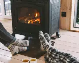 Pies con calcetines calentándose junto a una estufa de leña, disfrutando de la calefacción sin electricidad y una taza de té.
