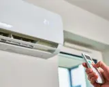 Mano con mando a distancia, ajustando la temperatura en el aire acondicionado para activar la bomba de calor.