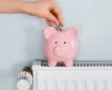 Mano inserta moneda en hucha rosa sobre radiador blanco. Ahorrando energía cuando se apaga la calefacción central.