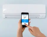 Mano ajustando la temperatura del aire acondicionado desde el móvil, facilitando conectar aire acondicionado a wifi para control remoto.