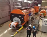 Dos técnicos observan varios tipos de calderas industriales naranjas y grises en una fábrica.