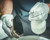Manos enguantadas sostienen cepillo y spray. Preparación para la limpieza de estufa de pellets, consulta el precio limpieza estufa pellets.