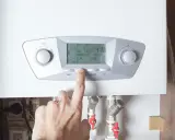 Un dedo presiona un botón en una caldera moderna, indicando el futuro de las calderas de gas y su control inteligente.