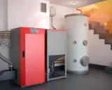Moderna caldera de pellets roja y gris junto a un gran acumulador de agua. Una solución eficiente para cambiar caldera de gas por pellets.