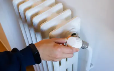 Mano ajustando el termostato de un radiador, controlando la calefacción central en comunidades de vecinos para un confort óptimo.