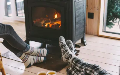 Pies con calcetines calentándose junto a una estufa de leña, disfrutando de la calefacción sin electricidad y una taza de té.