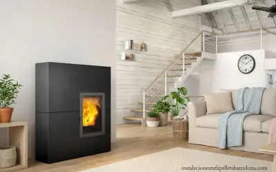 Estufa de pellets negra con fuego encendido, junto a escaleras y sofá. Ideal para un esquema de instalación de hidroestufas de pellets.