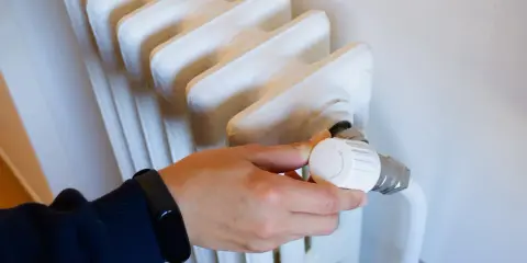 Mano ajustando el termostato de un radiador, controlando la calefacción central en comunidades de vecinos para un confort óptimo.