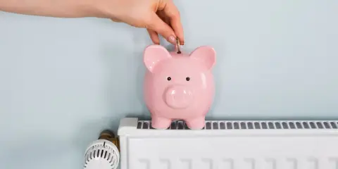 Mano inserta moneda en hucha rosa sobre radiador blanco. Ahorrando energía cuando se apaga la calefacción central.
