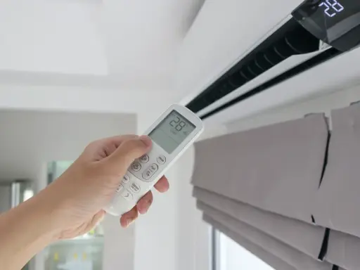 Mano sujetando control remoto de aire acondicionado, mostrando la diferencia entre climatizador y aire acondicionado.