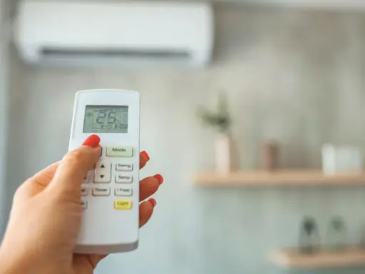 Mano con control remoto ajustando el aire acondicionado, buscando la temperatura ideal.