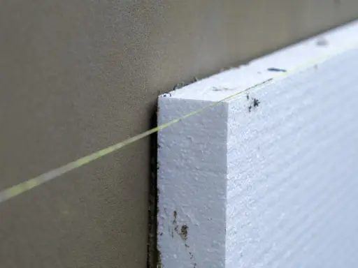Instalación de aislamiento térmico para aislar tubos de calefacción exterior. Una línea guía de color amarillo ayuda a colocar el poliestireno.