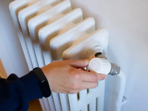Mano ajustando el termostato de un radiador, controlando la calefacción central en comunidades de vecinos para un confort óptimo.
