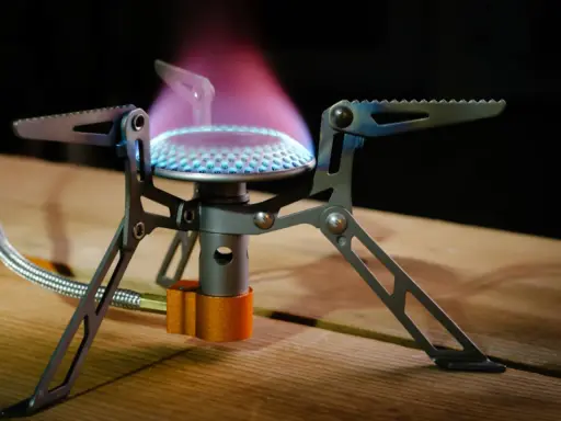 Estufa portátil sin electricidad ni gas, con llama azul y púrpura, ideal para acampar.